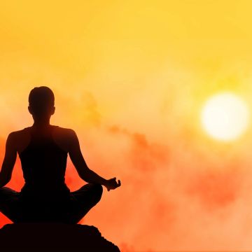 Silhouette of a person meditating at sunset with a vibrant orange sky.