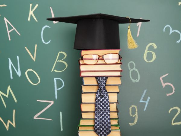 Stack of books dressed as a graduate with cap, glasses, and tie.