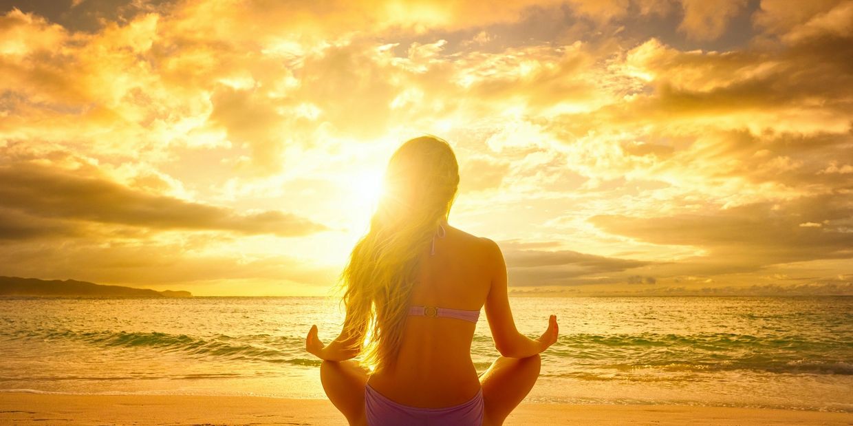 caucasian woman in seated meditation in front of a sunset on the beach