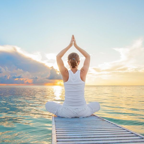 Photo of a woman sitting in meditation at the end of a pier looking out at the sea
