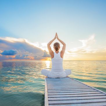Person meditating on a dock at sunrise over calm water.