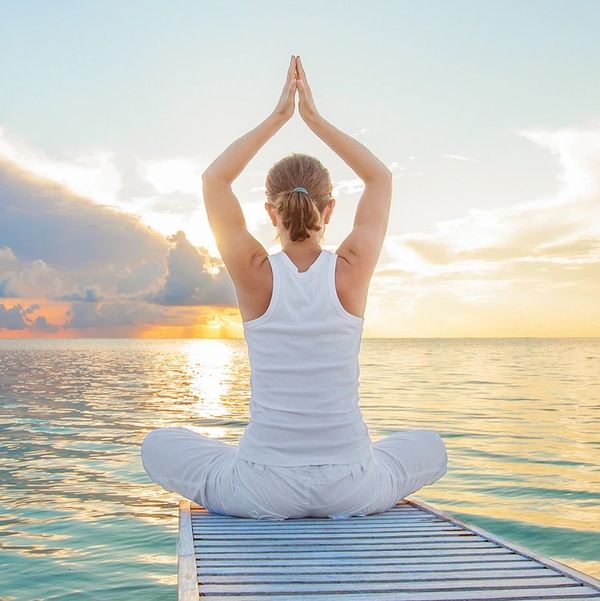 Photo of a woman sitting in meditation at the end of a pier looking out at the sea