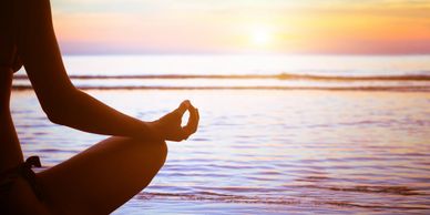 Person meditating by the sea at sunset.