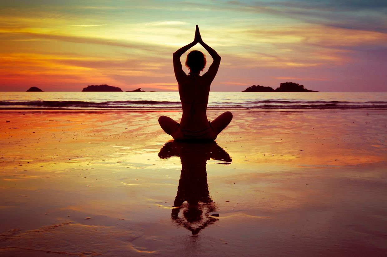 Silhouette of a person meditating on the beach at sunset.