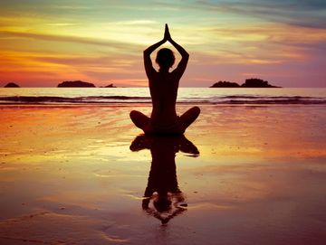 Person meditating on the beach at sunset.