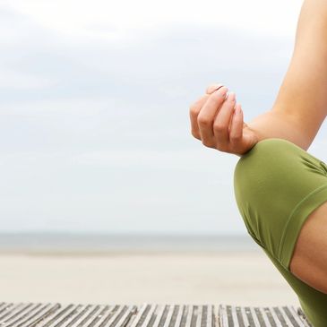 A person's leg, sitting cross-legged, with a hand resting on top of it as part of a yoga pose.