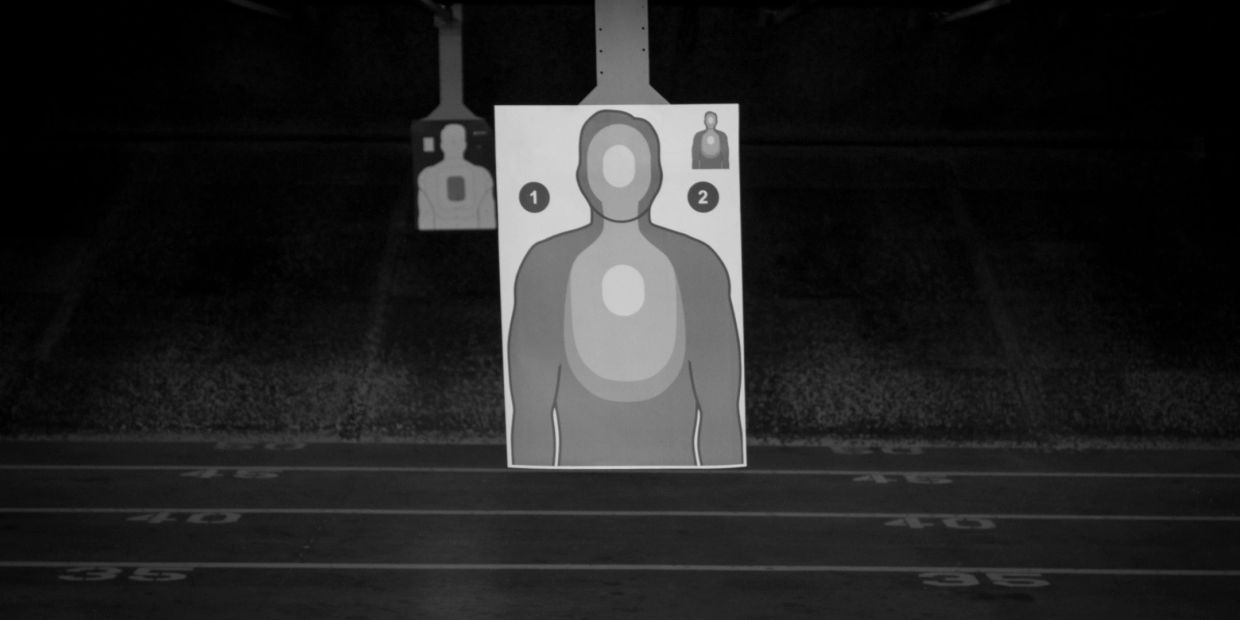 Gun range targets with silhouette bullseyes in a dimly lit shooting area.