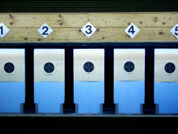 Indoor shooting range targets numbered 1 to 5 with bullet holes.