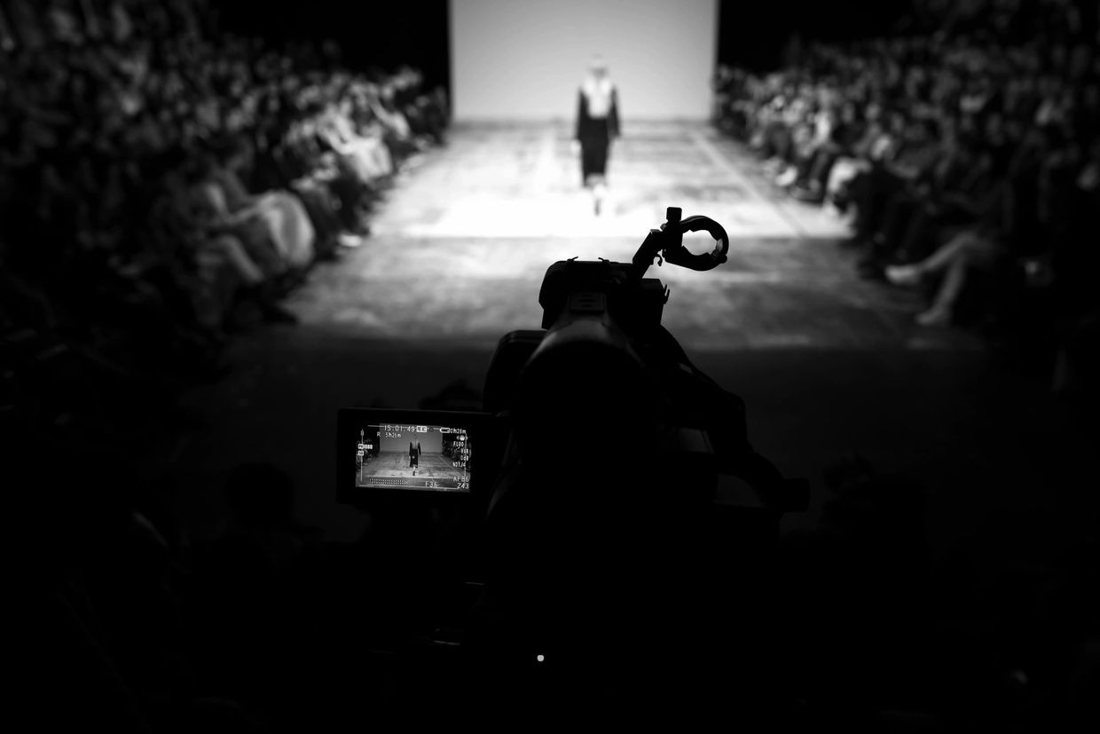 Camera filming a fashion runway show in black and white.