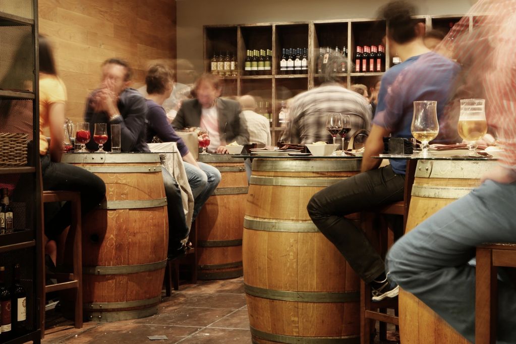 People enjoying drinks at a rustic bar with barrel tables and a warm ambiance.