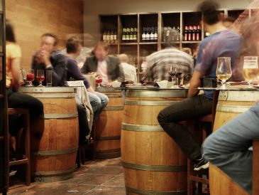 People enjoying drinks in a cozy bar with barrel tables.
