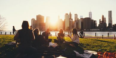 Group of friends enjoying a picnic at sunset with a city skyline in the background.