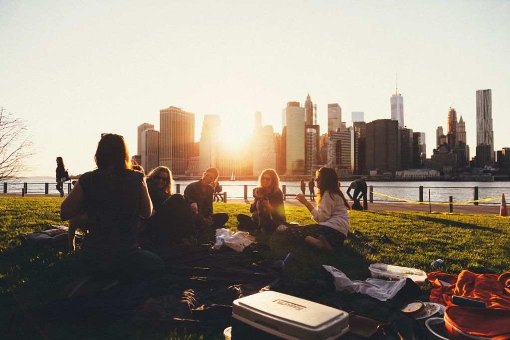 Friends enjoy a sunset picnic with a city skyline backdrop.
