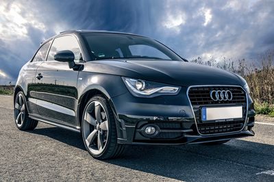 Black Audi parked on road under cloudy sky.