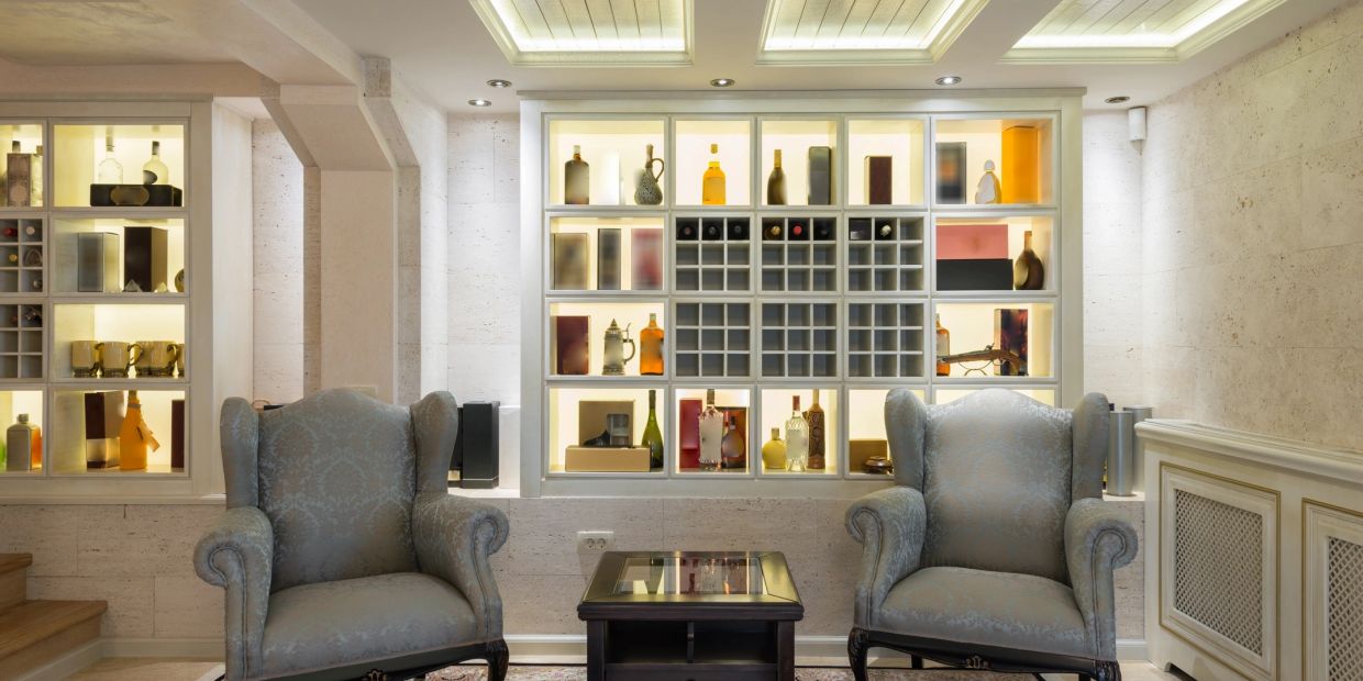Two armchairs in front of illuminated bottle shelves.