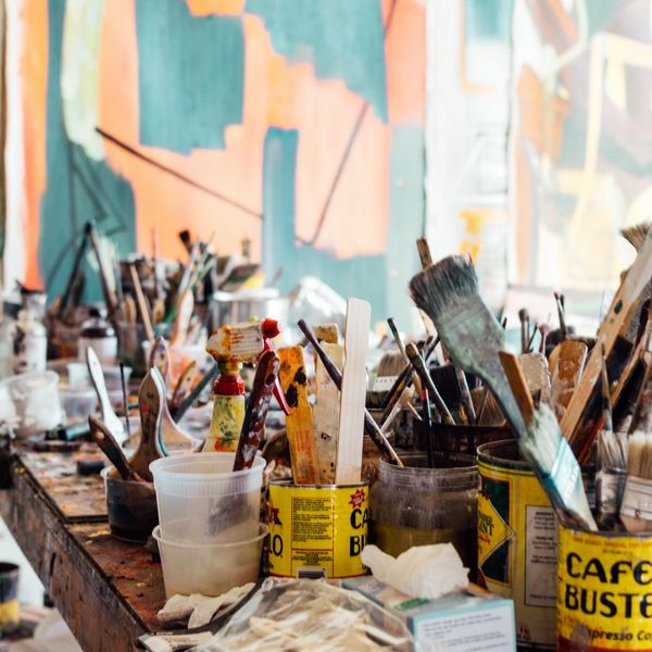 A cluttered artist's table filled with various paintbrushes and containers.