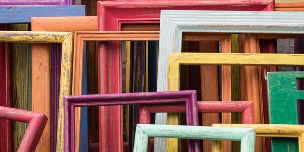 Large selection of different sizes, colours and styles of frames stacked against a wall.