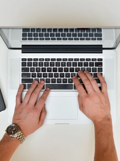 Hands typing on a laptop with a notebook, coffee, and smartphone nearby.