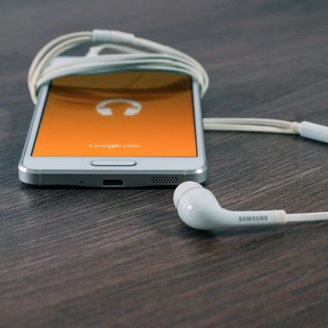 White Samsung Galaxy S-Series phone wrapped up in white Samsung brand earbuds and placed on a wood table.