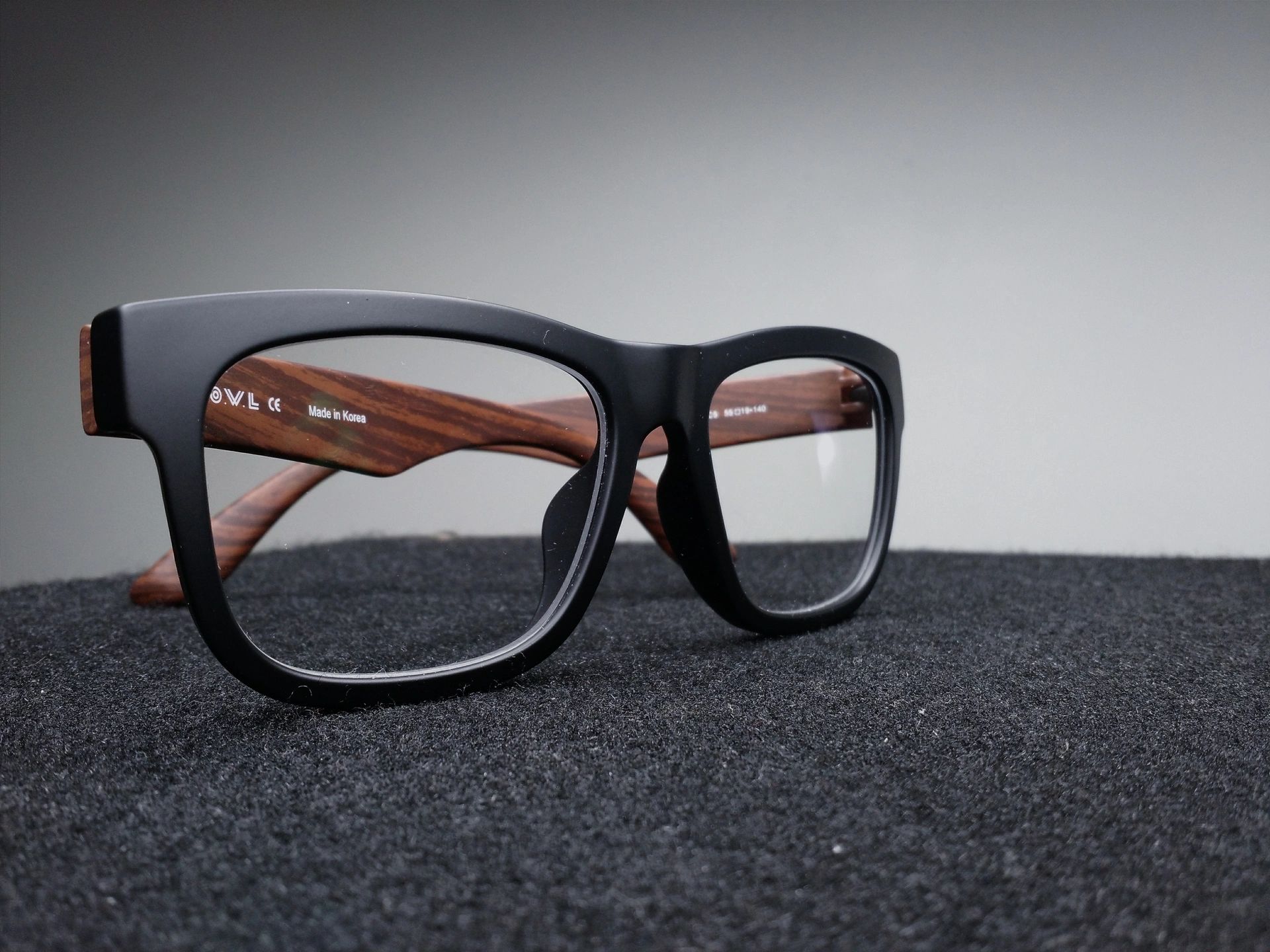 Black-framed glasses with wooden temples on a black surface.