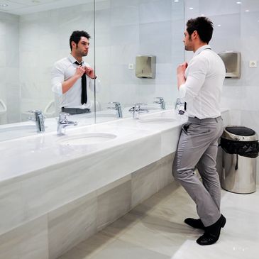 Man adjusting his tie in a modern white bathroom mirror.