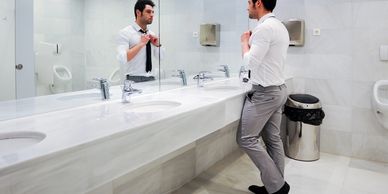 A man in a public restroom fixing his tie.