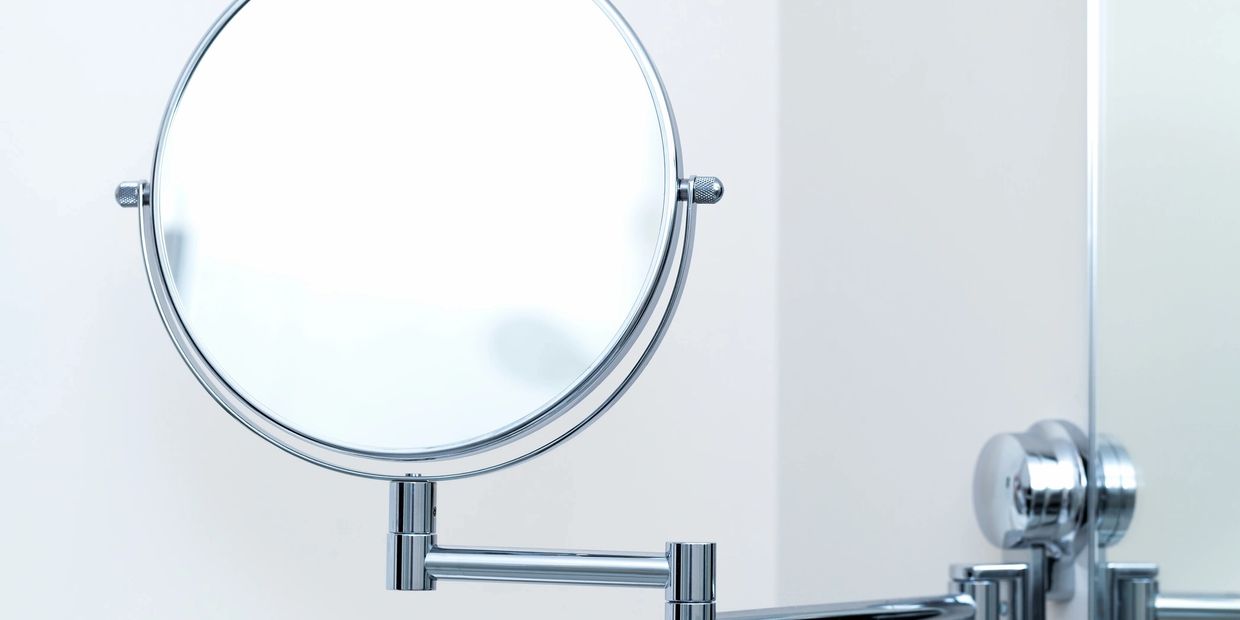 Shiny round bathroom mirror with adjustable arm mounted on wall.