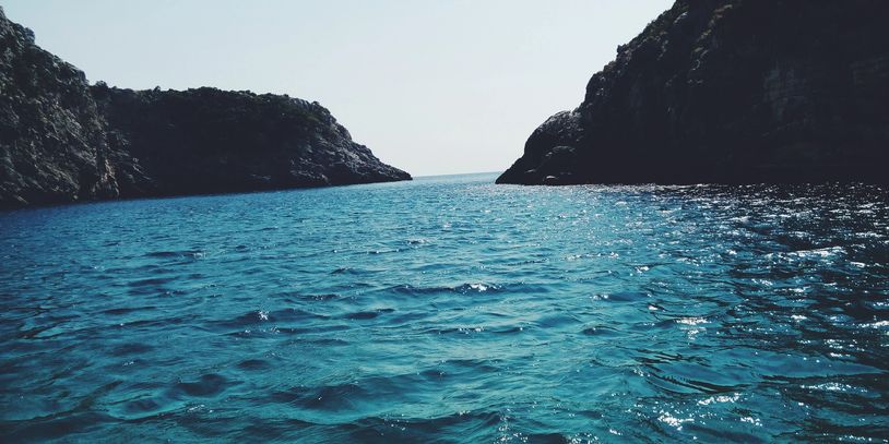 Blue sea water between two rocky cliffs under a clear sky.