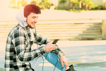 Young man enjoying music on phone outdoors.