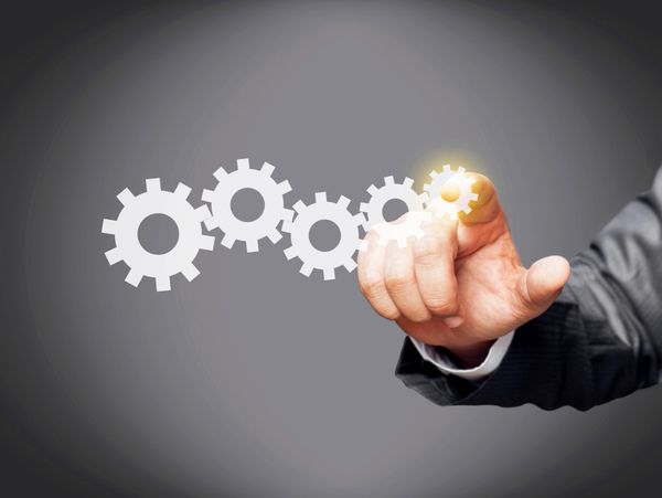 Hand in suit interacting with glowing gears representing teamwork.