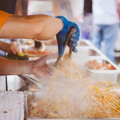 A person serving steaming hot noodles with tongs.