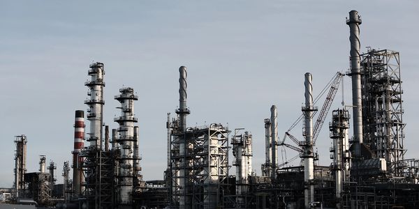 Industrial refinery with multiple tall chimneys and cranes under a cloudy sky.