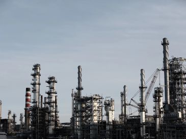 An industrial refinery complex with multiple tall smokestacks under a gray sky.