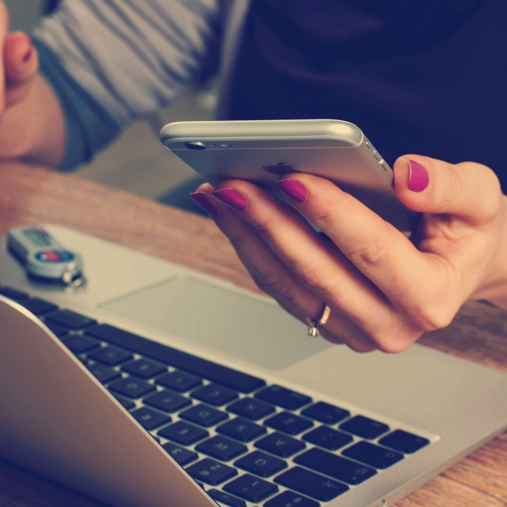 a lady holding an iPhone in front of a MacBook