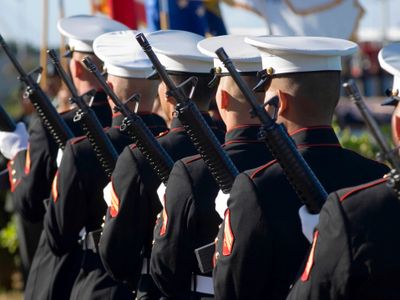 Marines in uniform standing in formation with rifles during a ceremony.