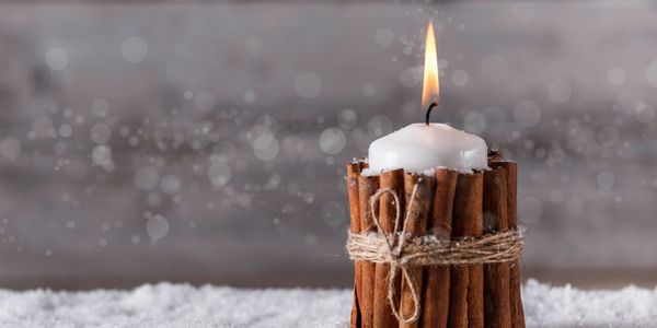 winter wonderland white candle with a cotton wick burning with cinnamon sticks wrapped around.