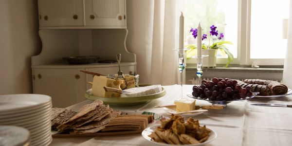 A cozy table set with assorted crackers, cheese, grapes, and candles near a window.