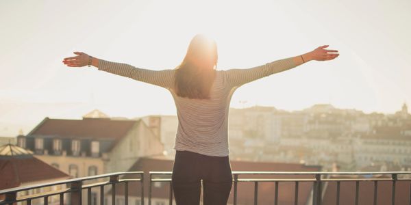 A woman standing outside in the sun with her hands raised in empowerment. 