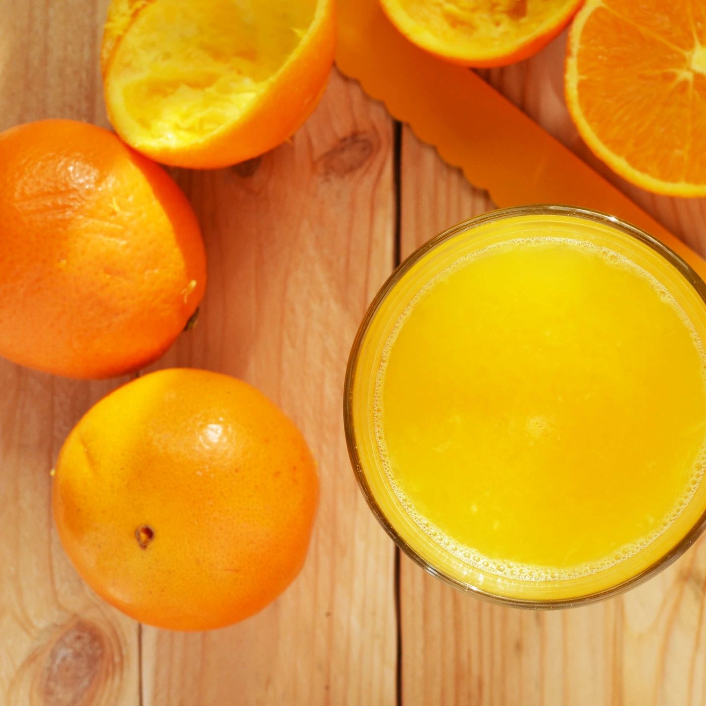 Freshly squeezed orange juice with whole and halved oranges on a wooden surface.