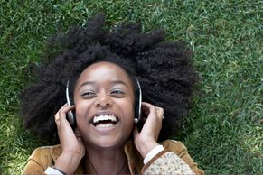 Young woman lying on grass, smiling with headphones on.