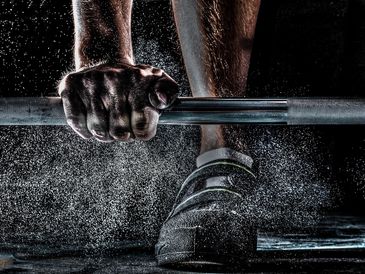 Close-up of hand gripping barbell with chalk dust.