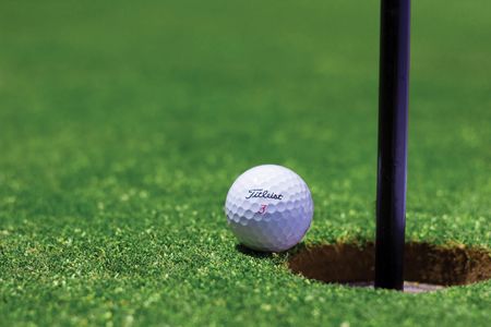 Golf ball next to the hole on green.