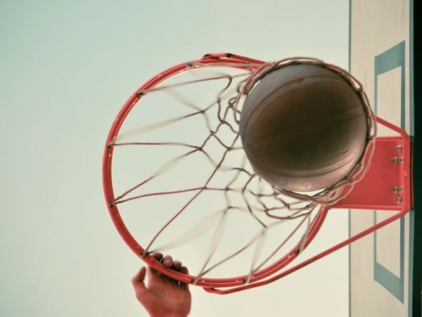 Basketball goes through the net while player hangs on rim.