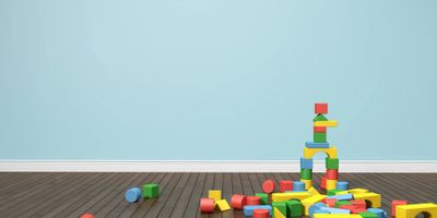 Colorful wooden blocks scattered and stacked on a wooden floor against a light blue wall.