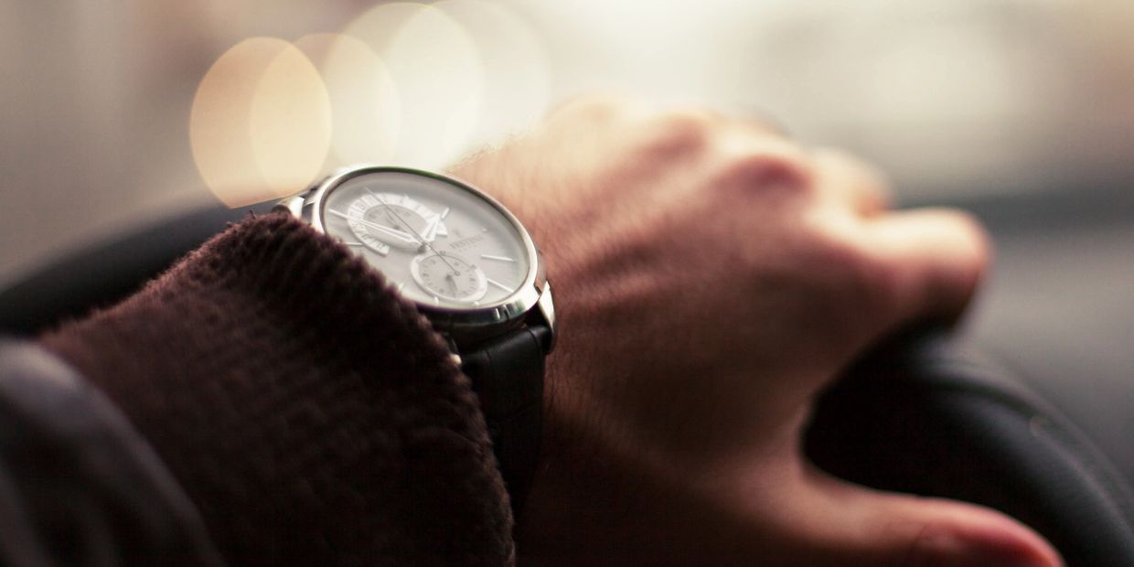 Close-up of a hand wearing a wristwatch holding a steering wheel.