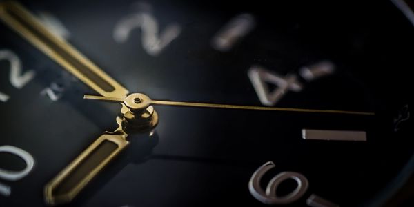 Close-up of a black watch face with gold hands and numbers.