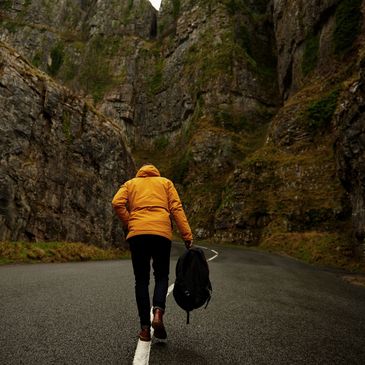 A person in a yellow jacket walking on a winding mountain road.