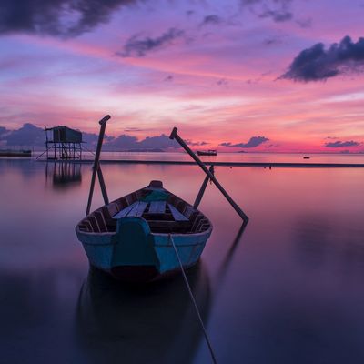 A boat anchored in calm water during a vibrant purple and pink sunset.