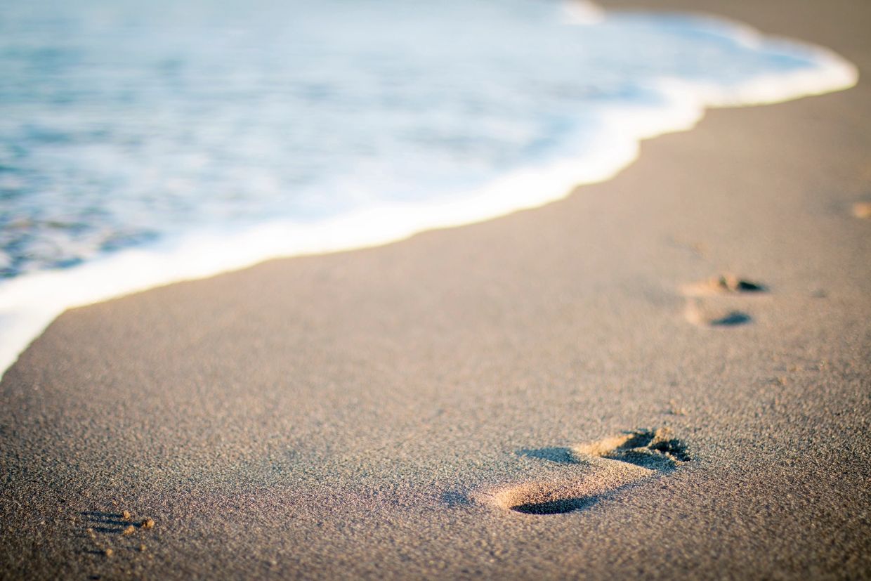 Footprints on sandy beach leading to the ocean's edge.