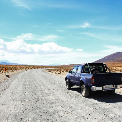 Blue pickup truck parked on a desert gravel road under a bright sky.